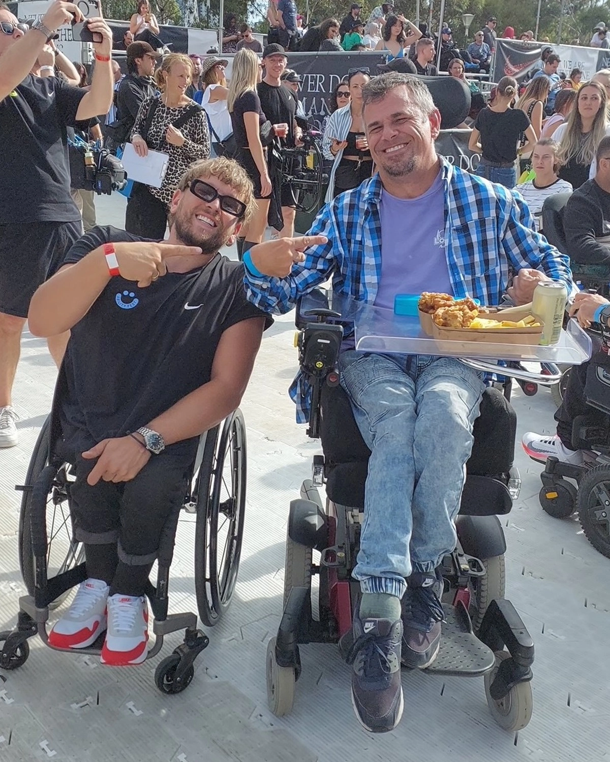 Two men using wheelchairs smile at an event atNDIS registered disability service Distinctive Options Independent living supports