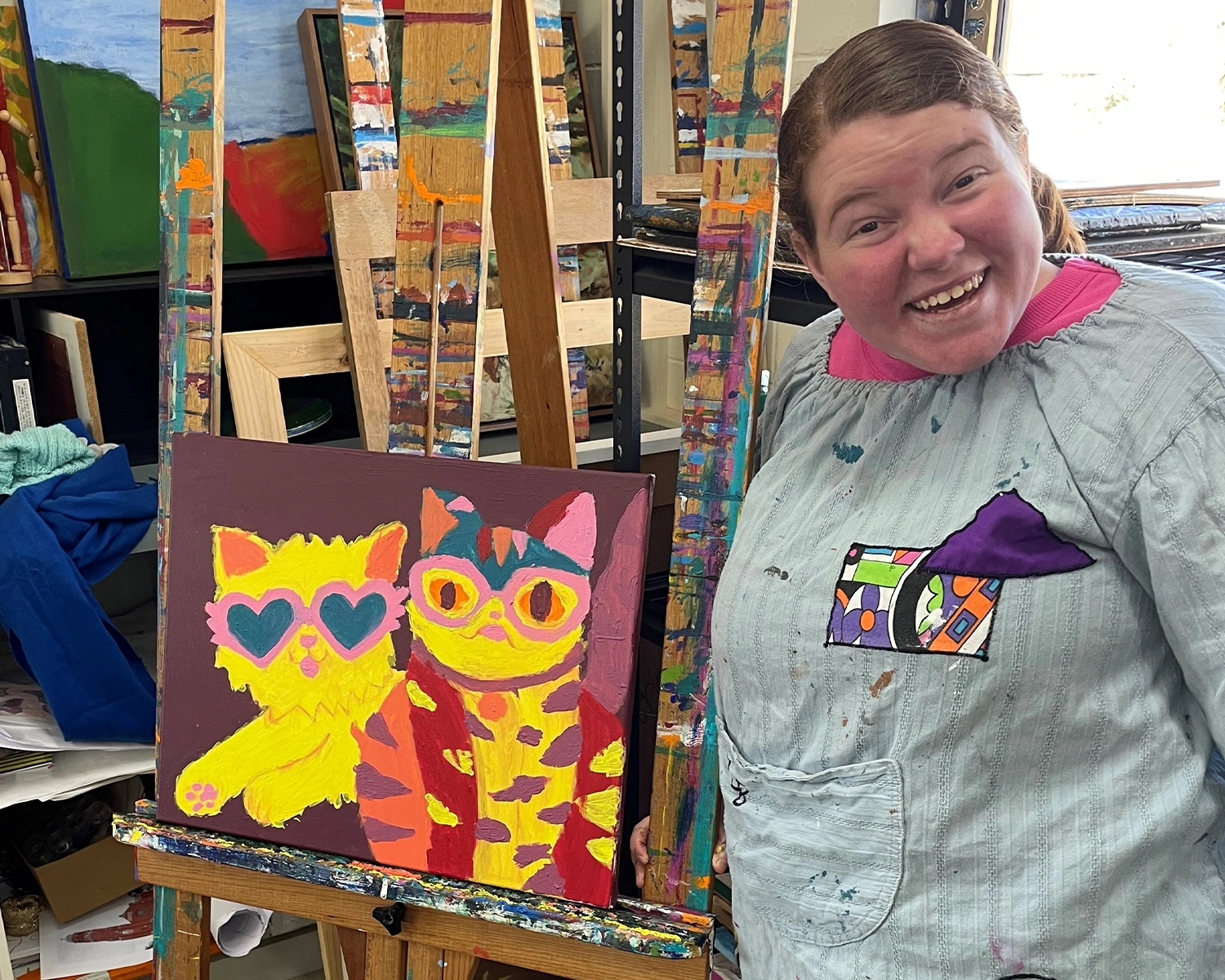 A woman stands smiling in front of a painting on an easel at Art at Distinctive Options Noweyung