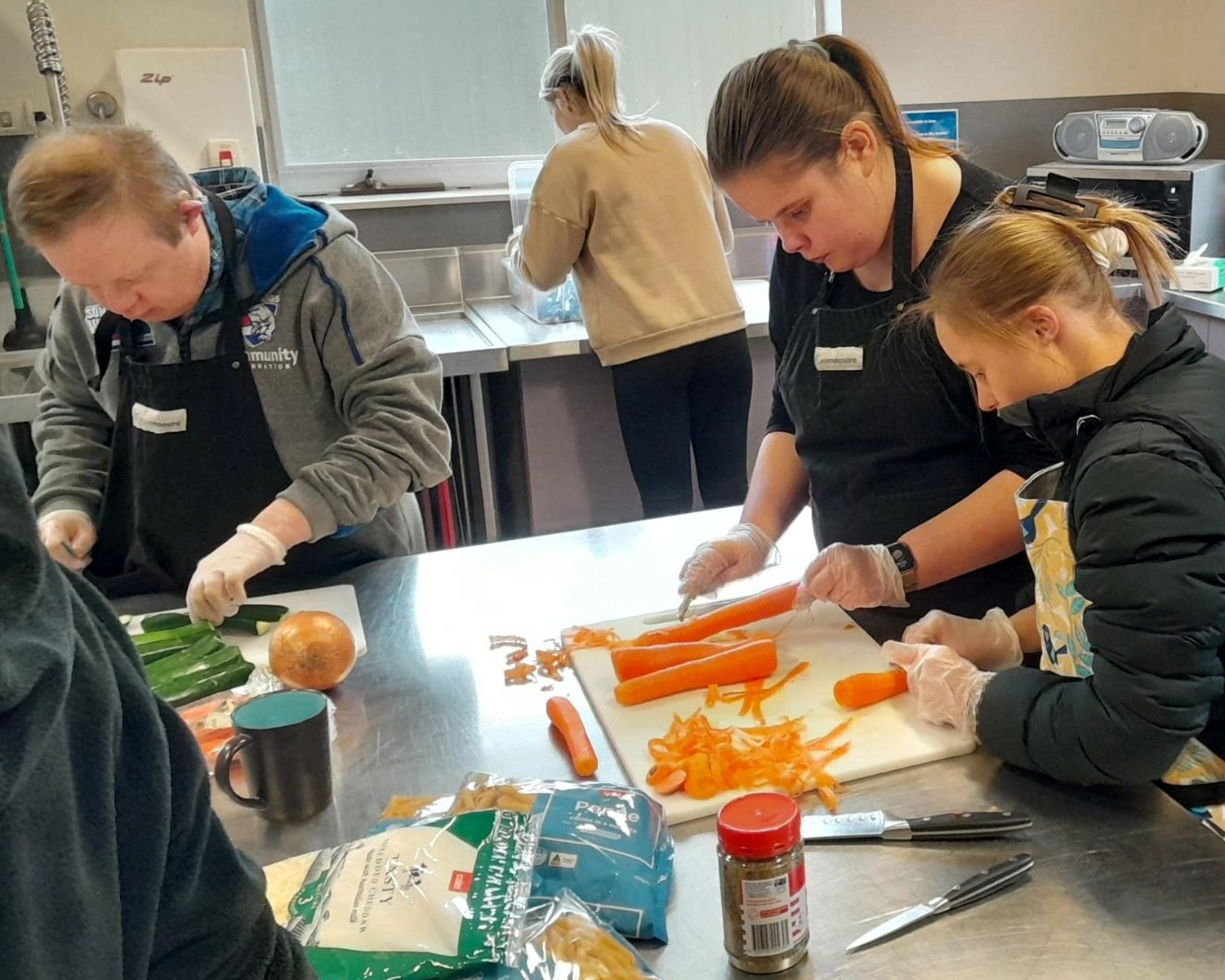 A group of people wearing aprons cut vegetables at NDIS registered disability service Distinctive Options