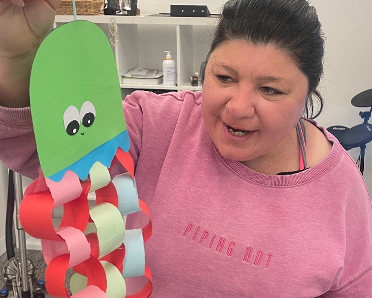 A woman golds up a paper craft sculpture and smiles at Brimbank Distinctive Options