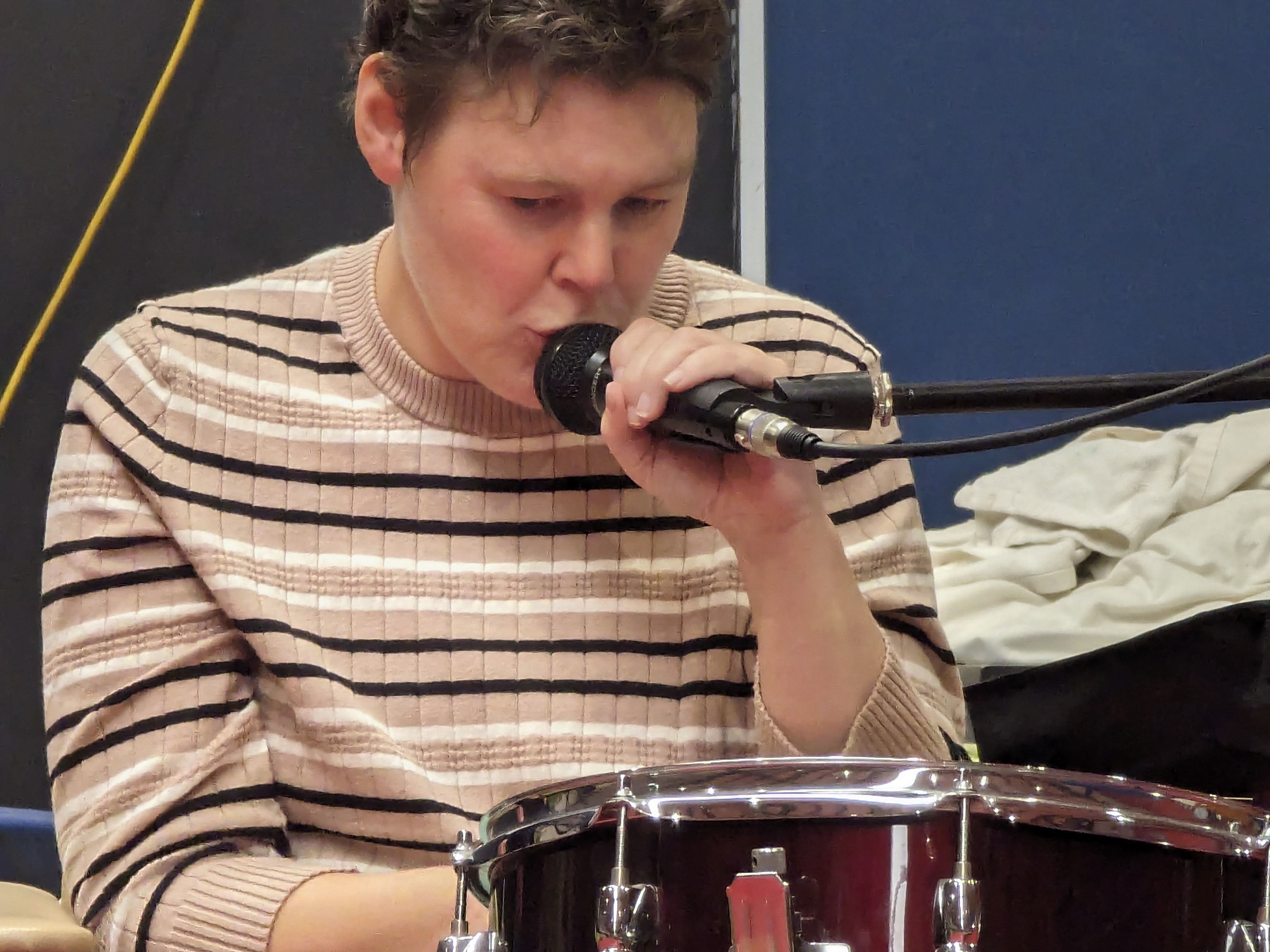 Lady singing into microphone while playing drums  at Distinctive Options Noweyung