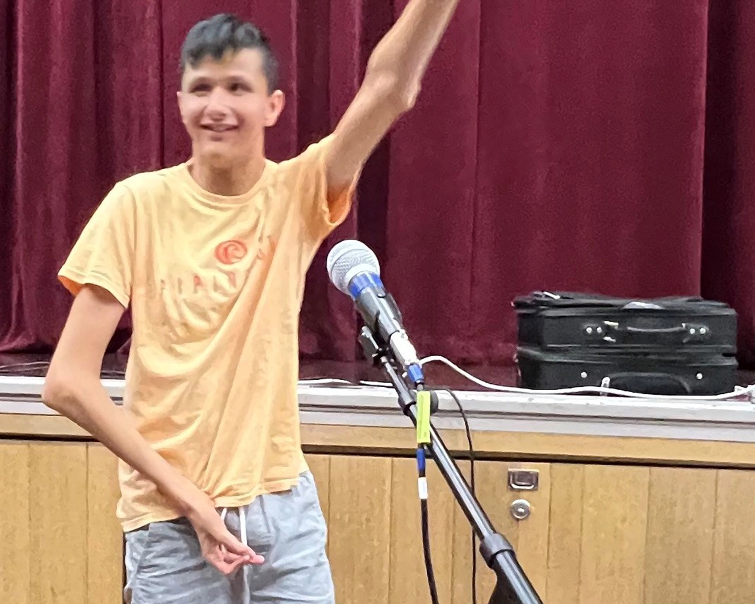A man performs in front of a stage with a microphone at a drama activity Distinctive Options