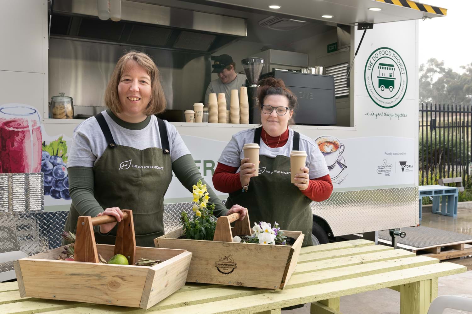 Two women wearing aprons stand in front of a food truck at Distinctive Options