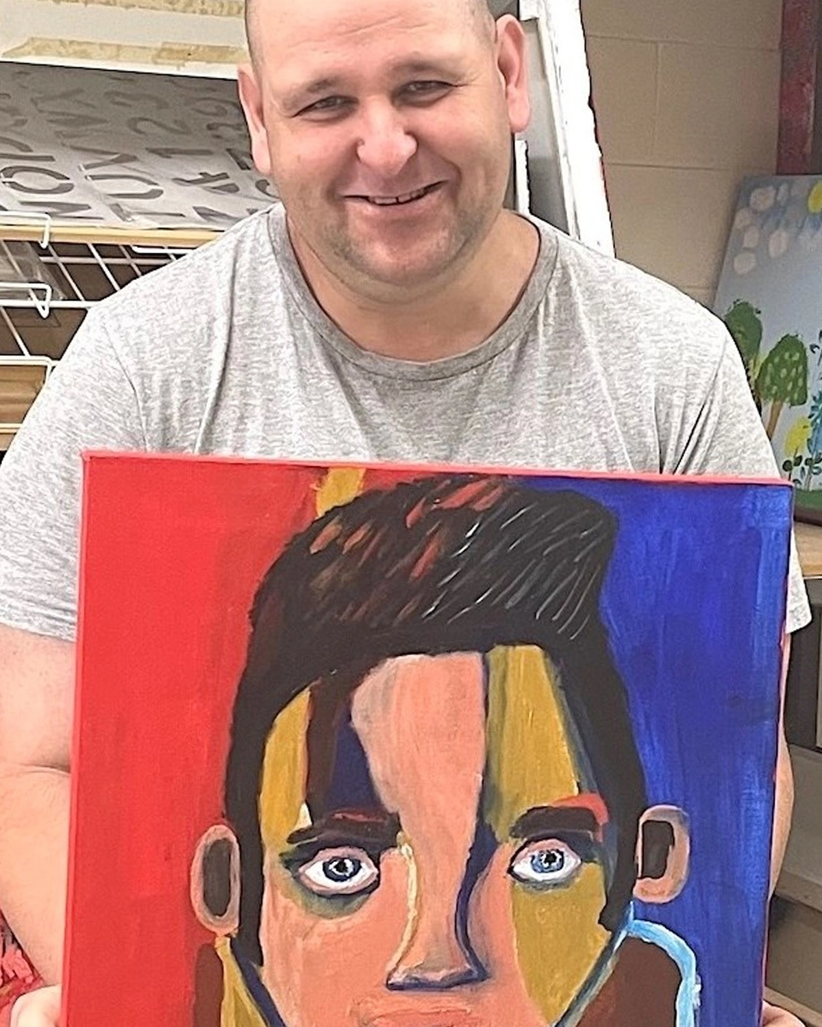 A man holds up a painting of Elvis Presley at NDIS registered disability service Distinctive Options