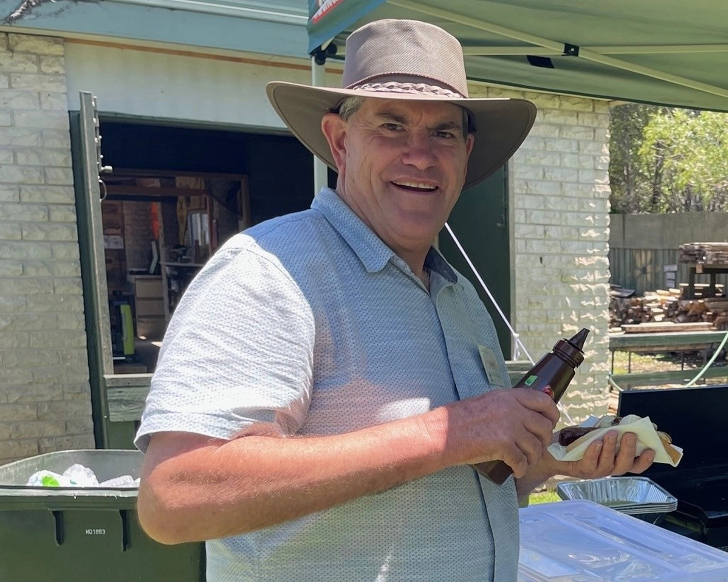 A man wearing a hat holds a sausage sandwich in his hand at Group Supports Mens Group at Distinctive Options Noweyung