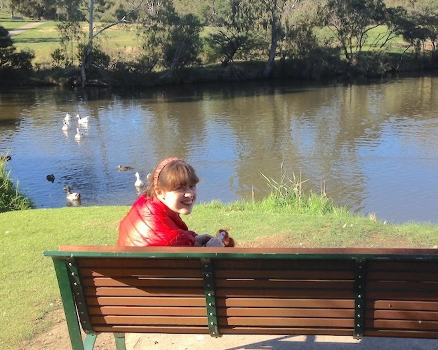 A woman sits on a park bench by a river at NDIS registered disability service Distinctive Options