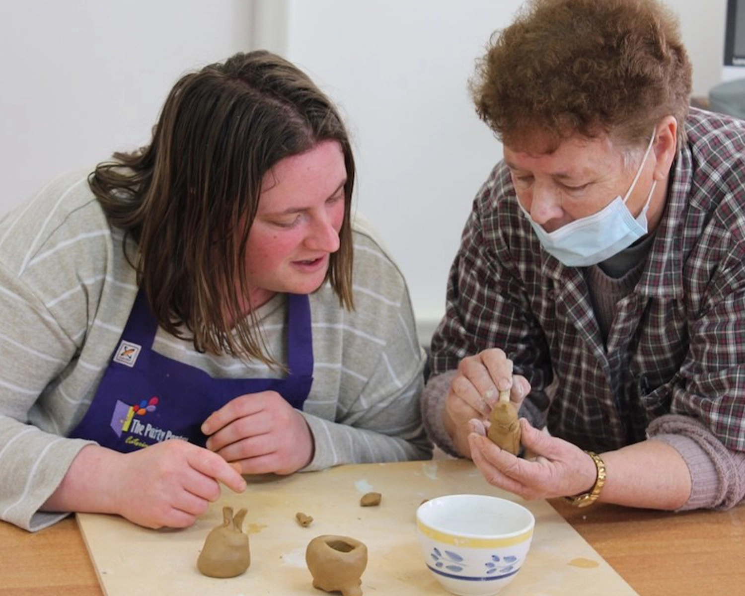 a worker shows a woman how to shape clay at NDIS registered disability service Distinctive Options