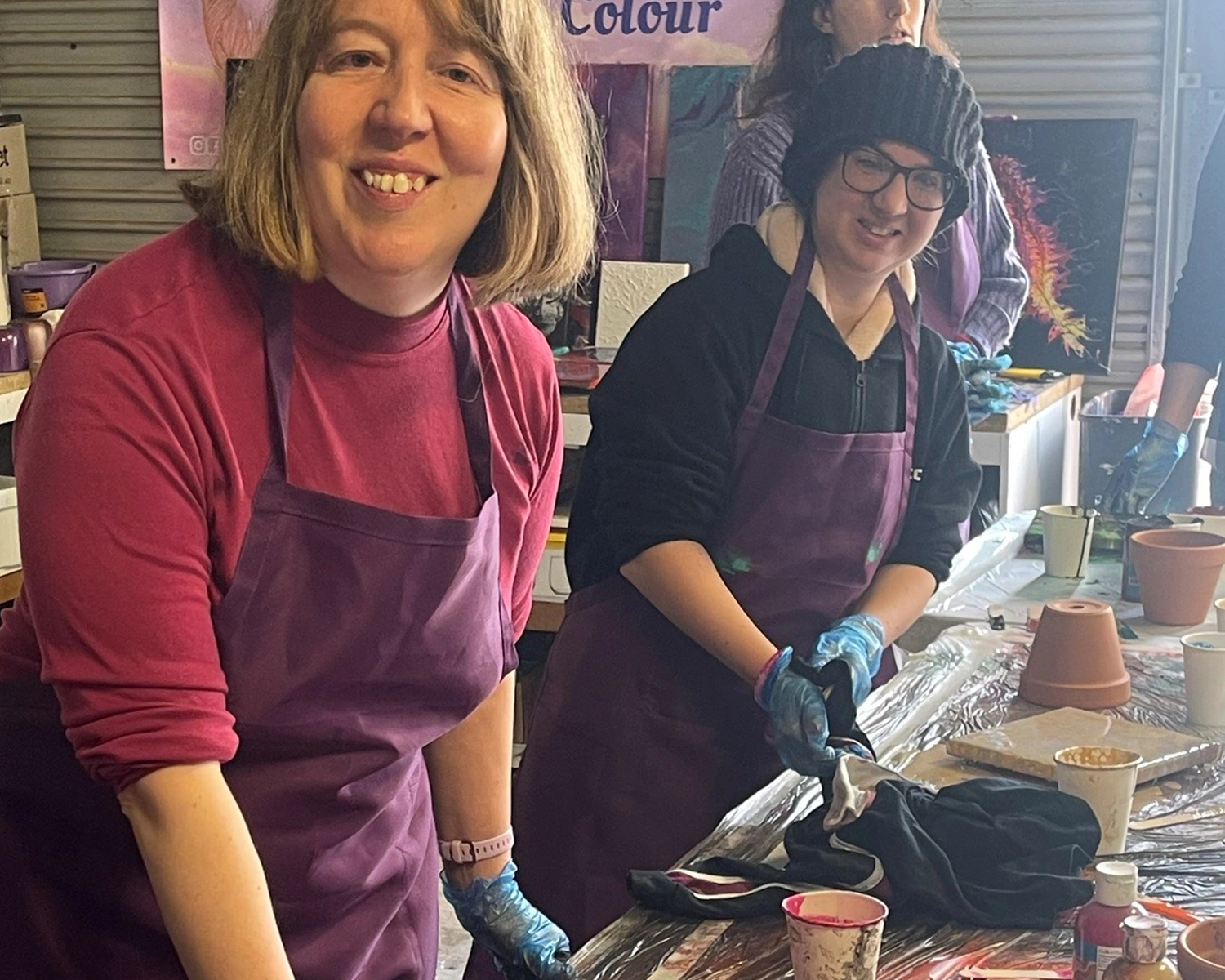 Two women wear aprons while paintingNDIS registered disability service Distinctive Options