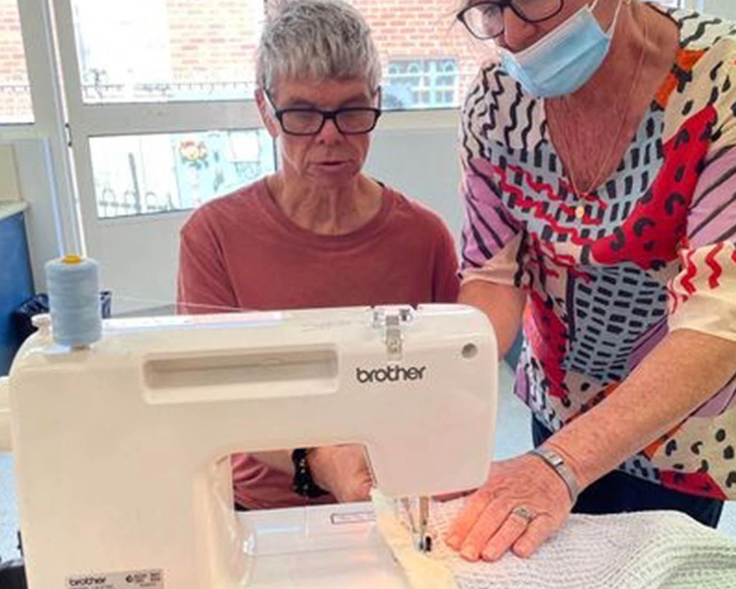 A man operates a sewing machine with a woman helping at NDIS registered disability service Distinctive Options