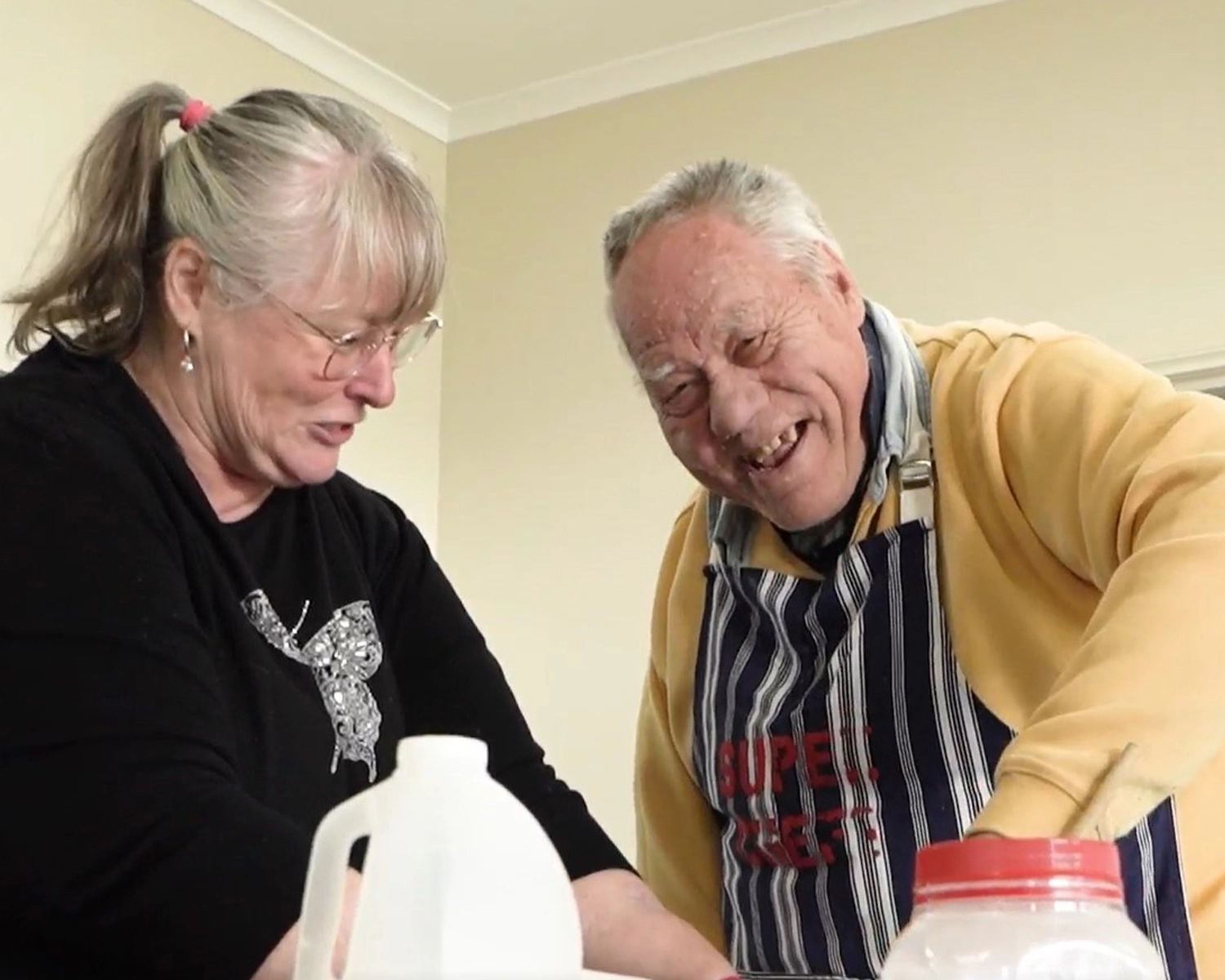 A man and a woman smile while wearing aprons and working in a kitchen, Building Independent Living skills 