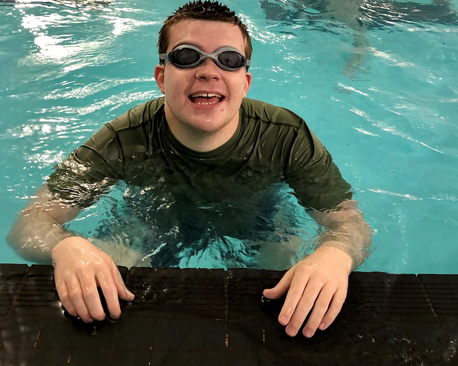 A man stands smiling in a swimming pool while wearing swimming goggles