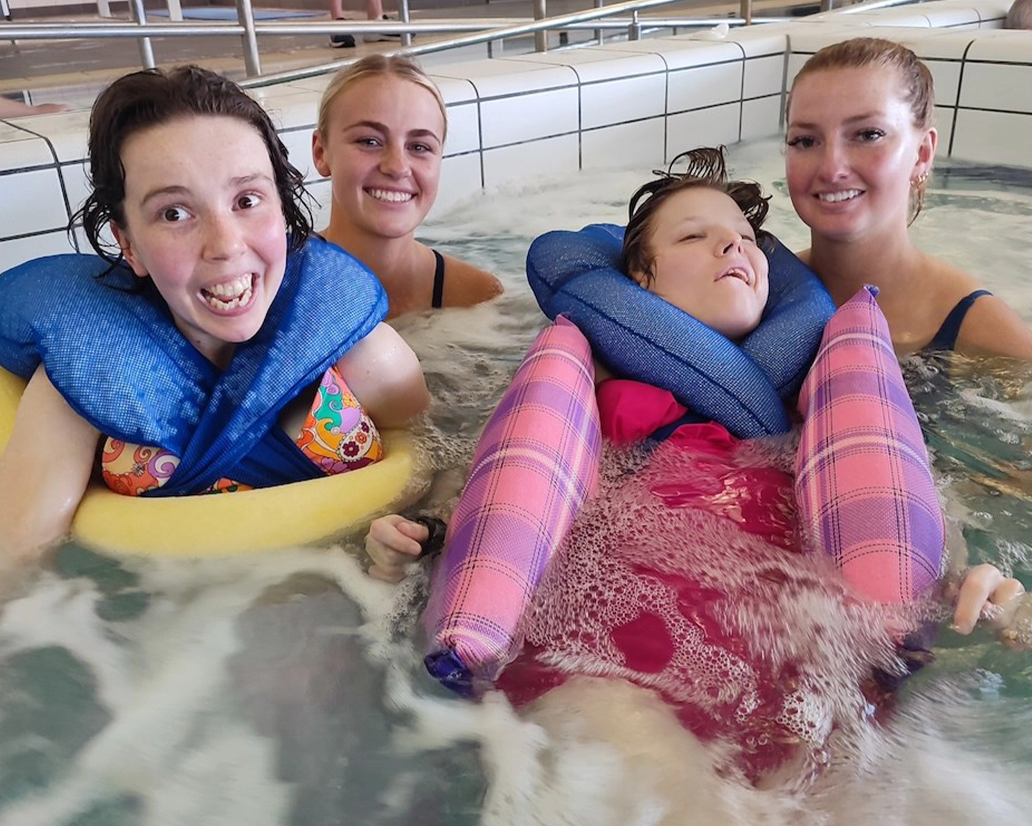 Two swimmers in a pool have support from two workers atNDIS registered disability service Distinctive Options