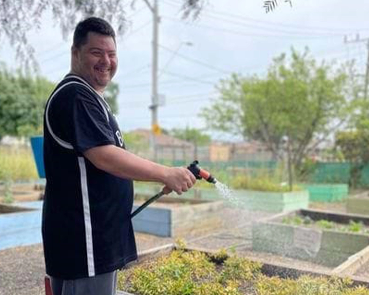 A man hoses a vegetable garden bed at NDIS registered disability service Distinctive Options